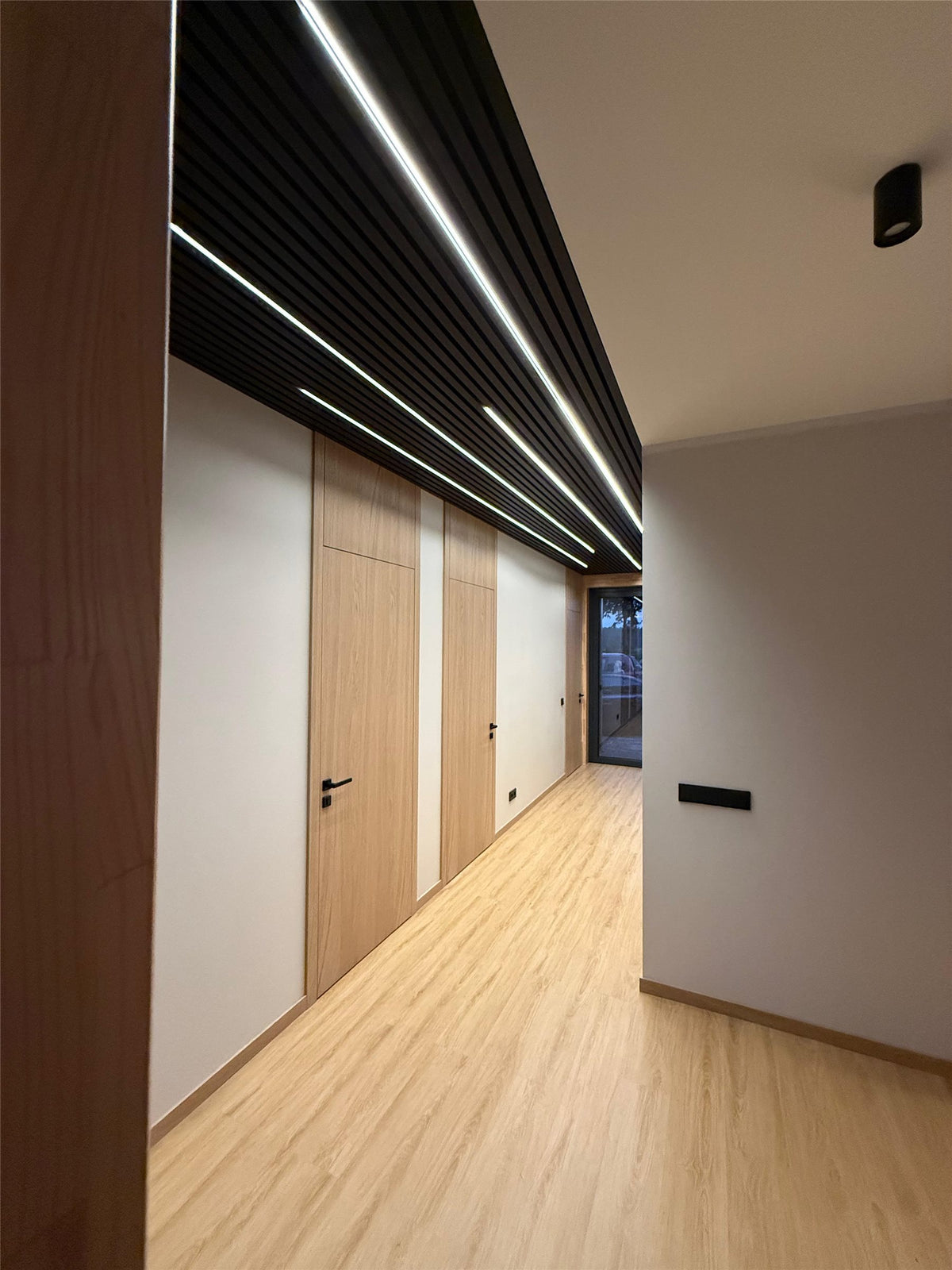Hallway with an anthracite slat acoustic ceiling and wall lined with light strips