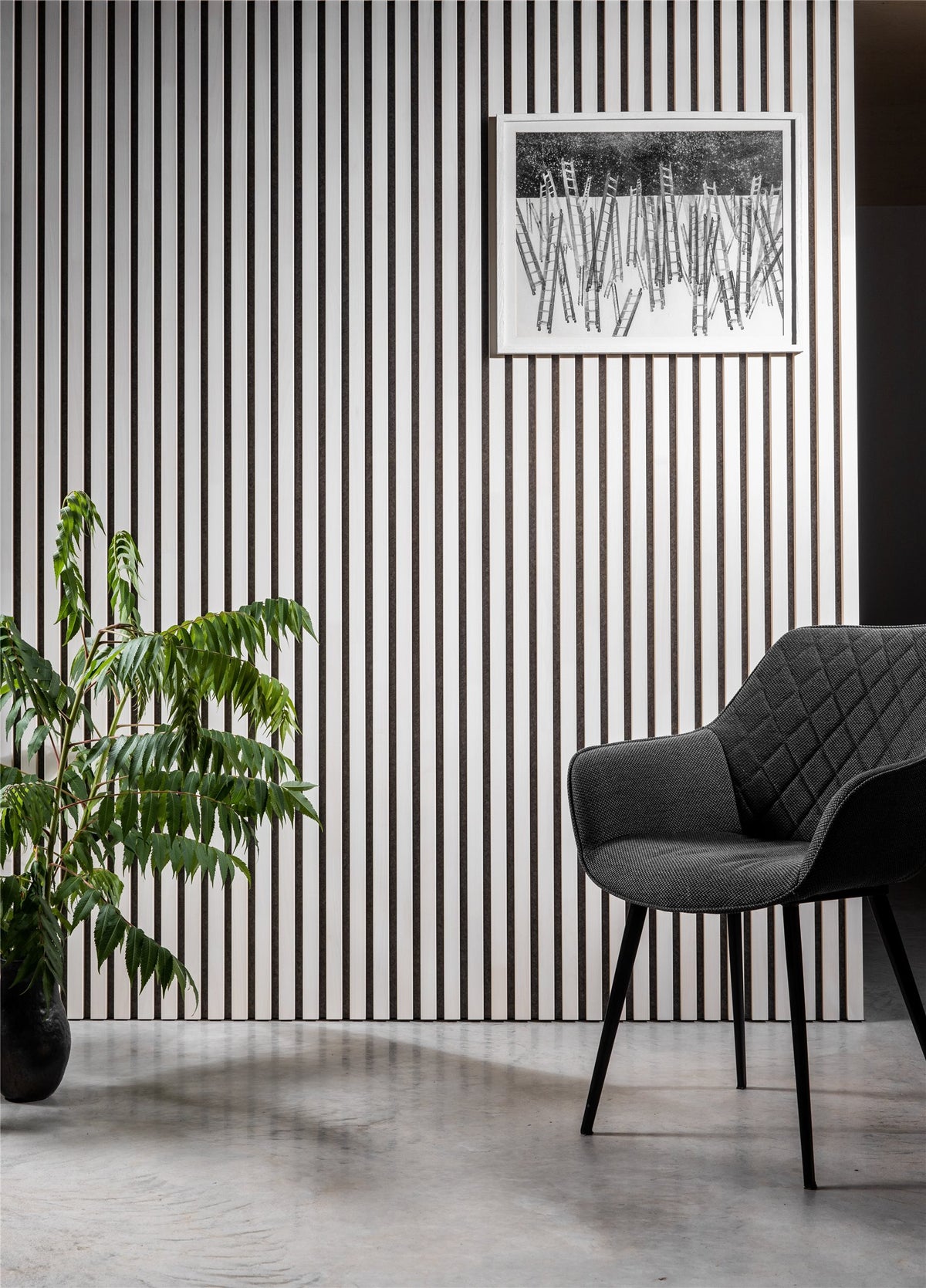 White slat acoustic wall with a black armchair and a pot plant
