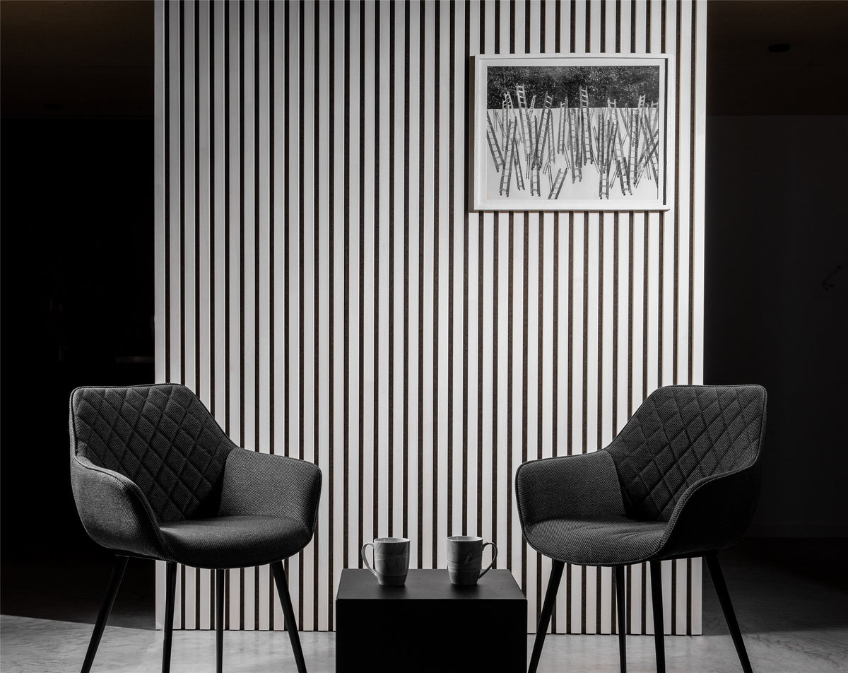 White slat acoustic wall with two black armchairs in a modern room