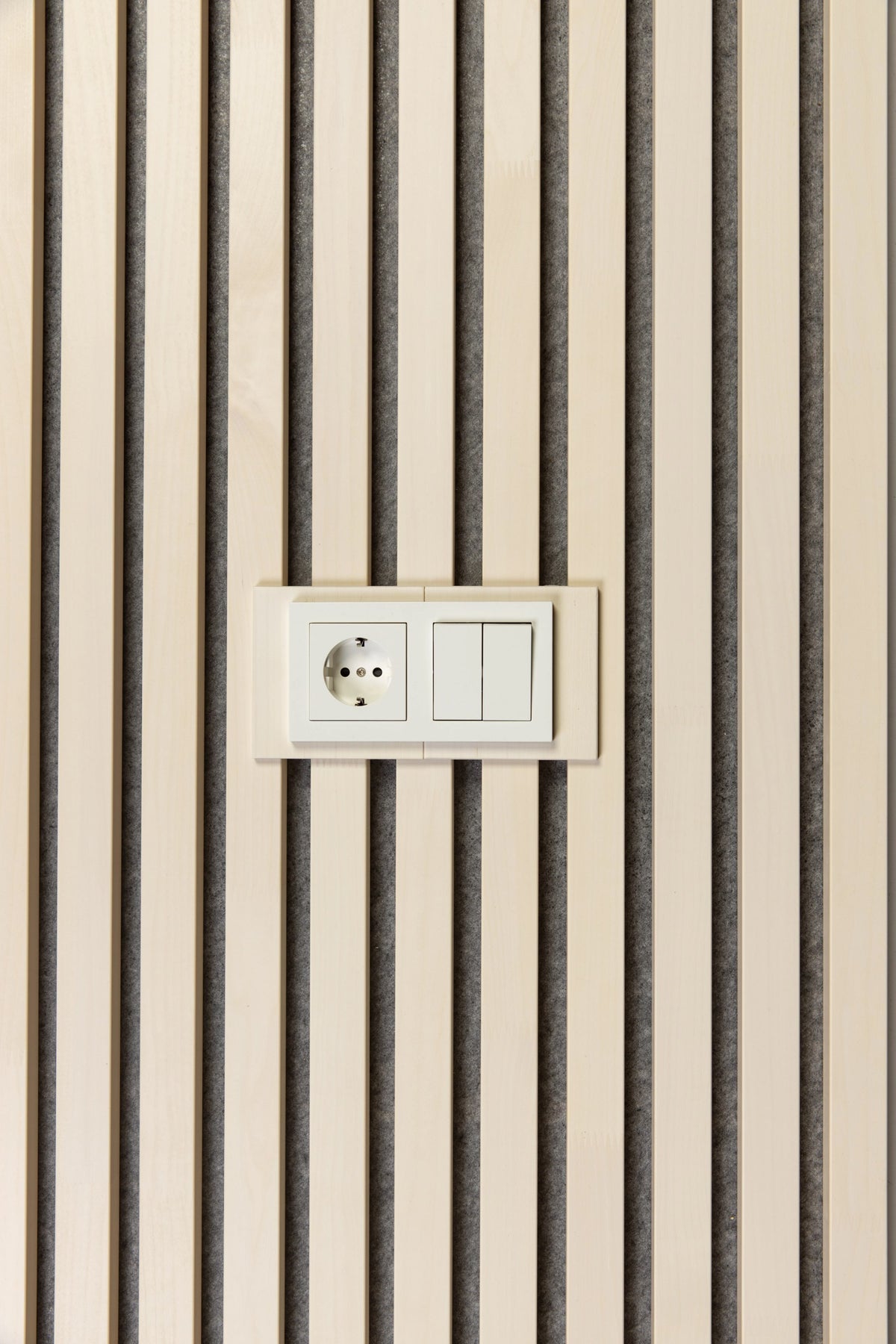 White plates around a wall socket and a double light switch on white aspen slats with grey felt